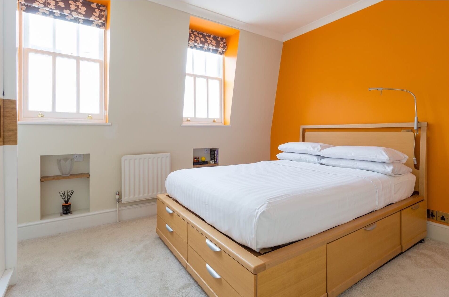 A bedroom with a bed, a radiator, a shelf, and a window.