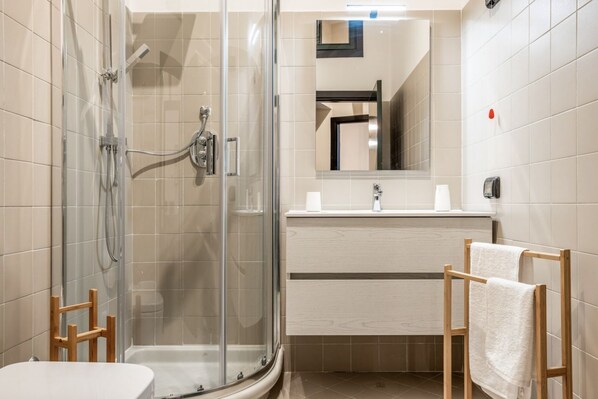 Une salle de bain moderne avec une douche à parois de verre, une chaise en bois, un lavabo avec un miroir et un porte-serviettes.