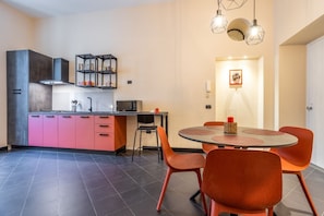 Une cuisine moderne avec des meubles roses, un coin repas avec des chaises orange et un sol carrelé en noir et blanc.