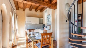 Un comedor con sillas de madera y una mesa de vidrio, una cocina con alacenas blancas y techo de madera.