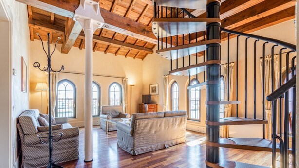 Un amplio salón con suelo de madera, una escalera en espiral y un gran ventanal.