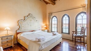 Un dormitorio con una cama grande, suelo de madera, ventanas arqueadas y una silla.