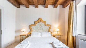 A hotel room with a wooden ceiling, a large bed with white linens, two bedside lamps, and a window with curtains.