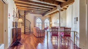 A spacious room with wooden flooring, a staircase, a dining area with chairs and a table, and two arched windows. - GuestHost - Molino Stucky Residence Galea Suite (Venezia)