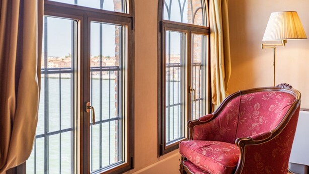 A room with large arched windows, a red upholstered chair, and a floor lamp. - GuestHost - Molino Stucky Residence Galea Suite (Venezia)
