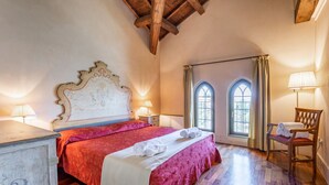 A bedroom with a wooden ceiling, a bed with a red bedspread, two bedside lamps, a chair, and a window with curtains. - GuestHost - Molino Stucky Residence Galea Suite (Venezia)