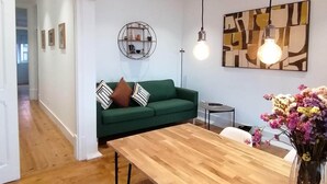 A modern living room with a green sofa, a wooden dining table, and a wall-mounted light fixture. - T2 w/ balcony (Lisboa)