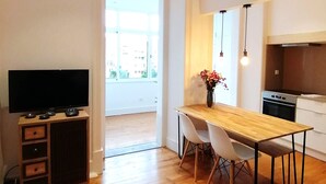 A modern kitchen with a wooden table, white chairs, a TV, and a vase of flowers. - T2 w/ balcony (Lisboa)