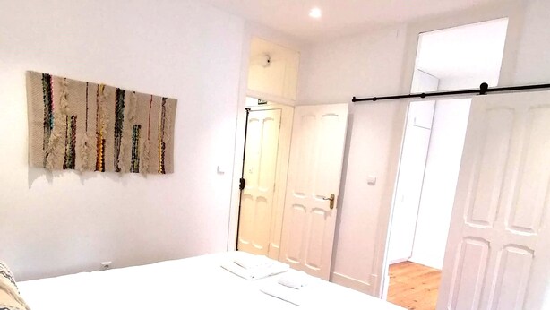A bedroom with a bed, a wall-mounted artwork, and a door leading to another room. - T2 w/ balcony (Lisboa)