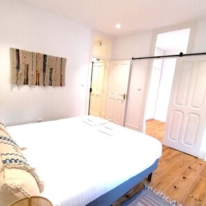 Quarto com uma cama, uma obra de arte na parede e uma porta que dá para outro espaço.