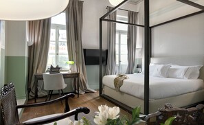 A four-poster bed, a desk with a chair, a television, and a window with curtains.