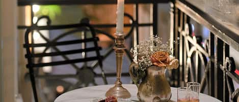 A round table with a candle, a vase with flowers, and two glasses on a balcony overlooking a cityscape.