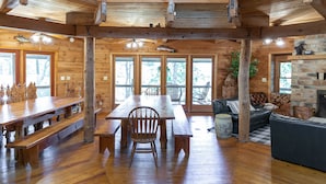 A wooden cabin interior with a large dining table, benches, a sofa, and a stone fireplace. - 15 Bedroom, Hot tub, Put Put, Pond, Pool Table (Needmore)