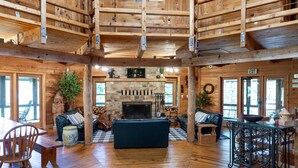 A log cabin interior with a stone fireplace, wooden floors, and a checkered floor mat. - 15 Bedroom, Hot tub, Put Put, Pond, Pool Table (Needmore)