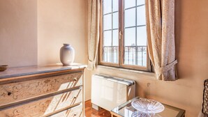 A room with a radiator, a glass table, a vase, and a window with curtains.
