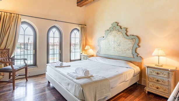 Un dormitorio con una cama grande, una silla de madera y una mesita de noche con lámparas.
