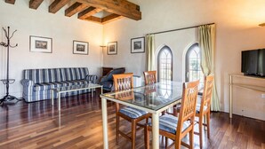 Un área de comedor con una mesa de vidrio, sillas de madera, un sofá a rayas y un televisor sobre un mueble.