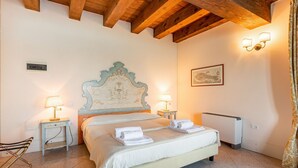 A hotel room with a bed, two bedside lamps, a radiator, a framed picture, and a wooden ceiling.