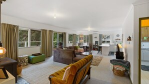 A spacious living room with a sofa, a green ottoman, and a dining area with a table and chairs. - Club Snowflake - Base of Buller (Sawmill Settlement)
