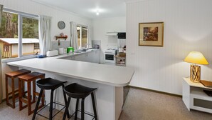 A kitchen with a white countertop, wooden stools, a sink, and a stove. - Club Snowflake - Base of Buller (Sawmill Settlement)