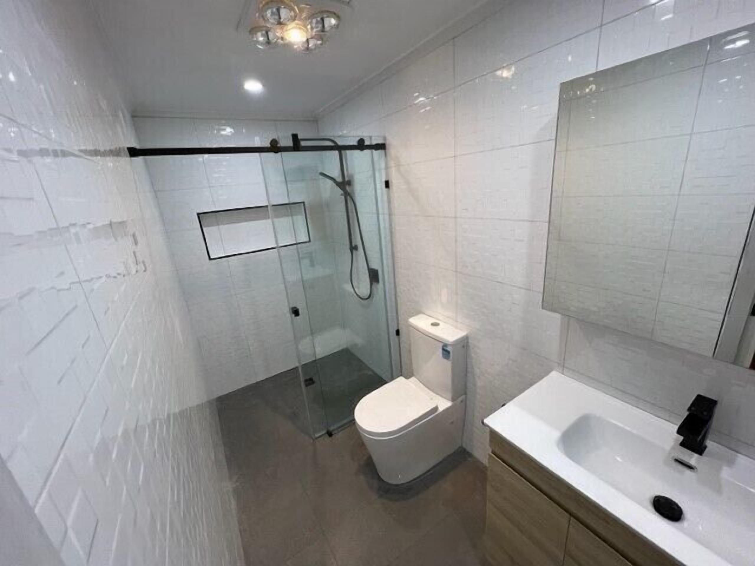 Et moderne badeværelse med brusekabine i glas, toilet og håndvask med spejl.