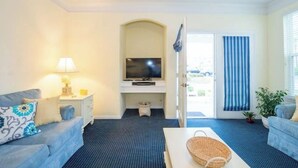 Une pièce avec un téléviseur posé sur un meuble, deux canapés, une petite table et une porte donnant sur l’extérieur.