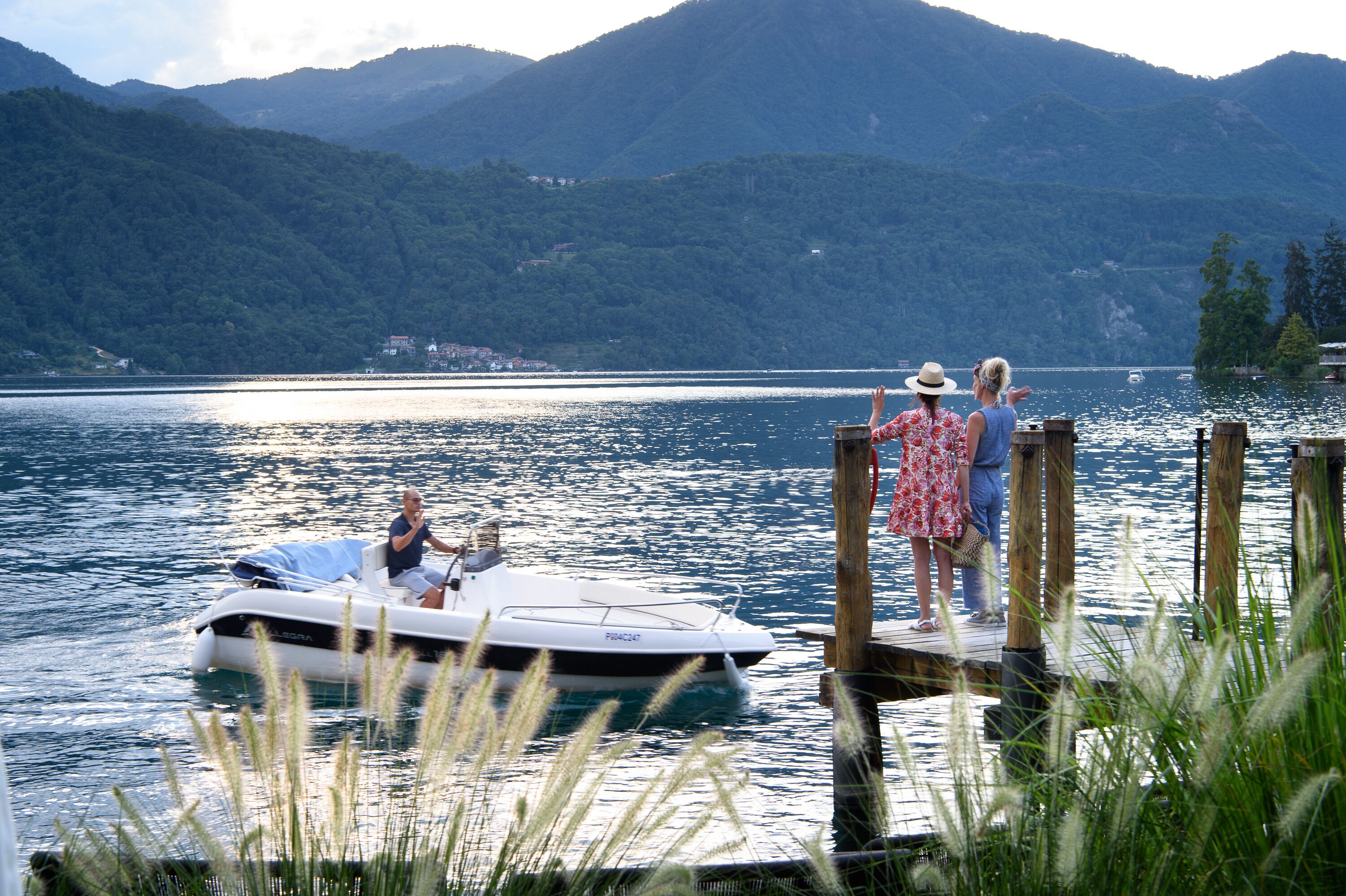 Un lac où un bateau est amarré à un quai en bois, entouré de montagnes et de verdure.
