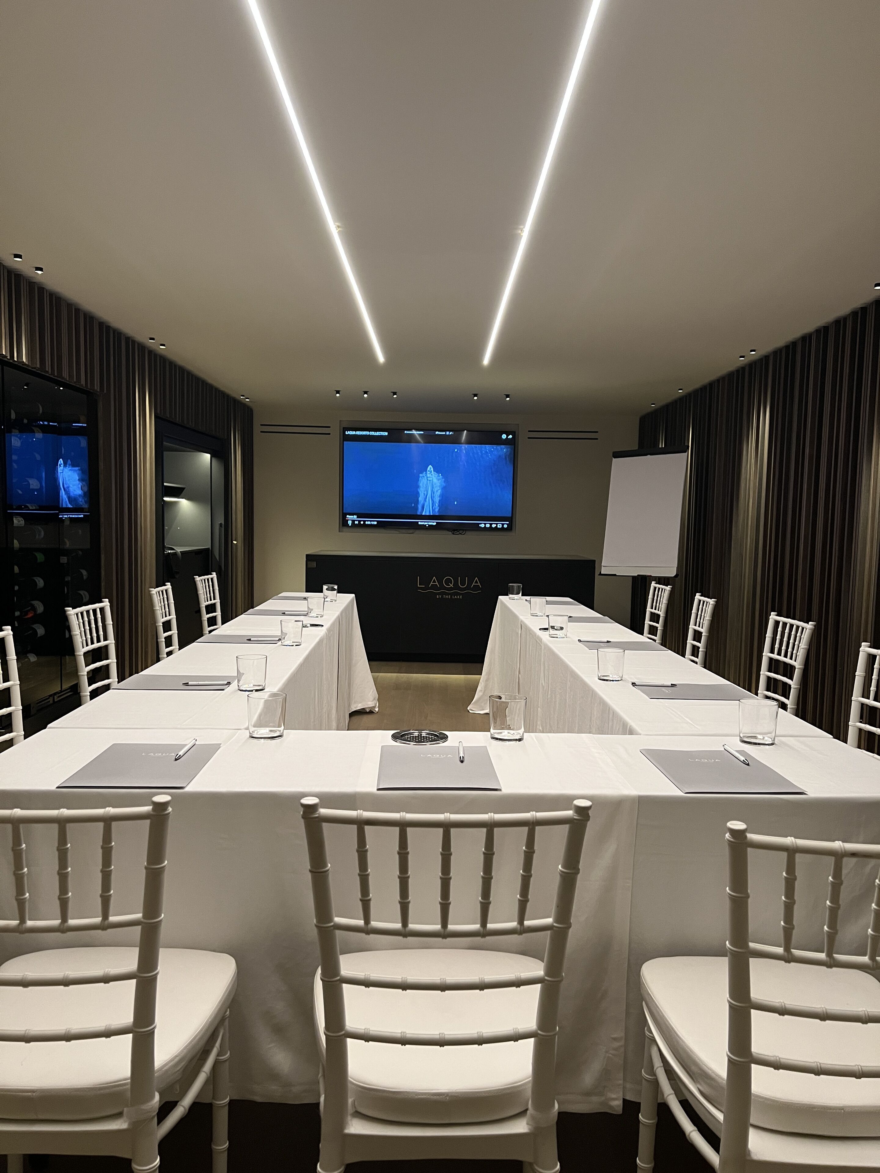 A conference room with a long table, chairs, a TV screen, and a whiteboard.