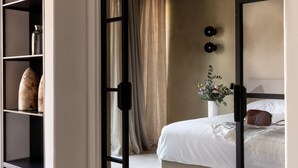 Een slaapkamer met een bed, nachtkastje, vaas met bloemen en een plank met decoratieve spullen.