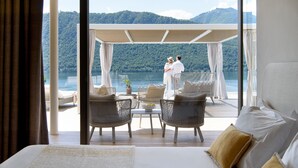 Een balkon met rieten meubels, een bed en uitzicht op een meer en bergen.