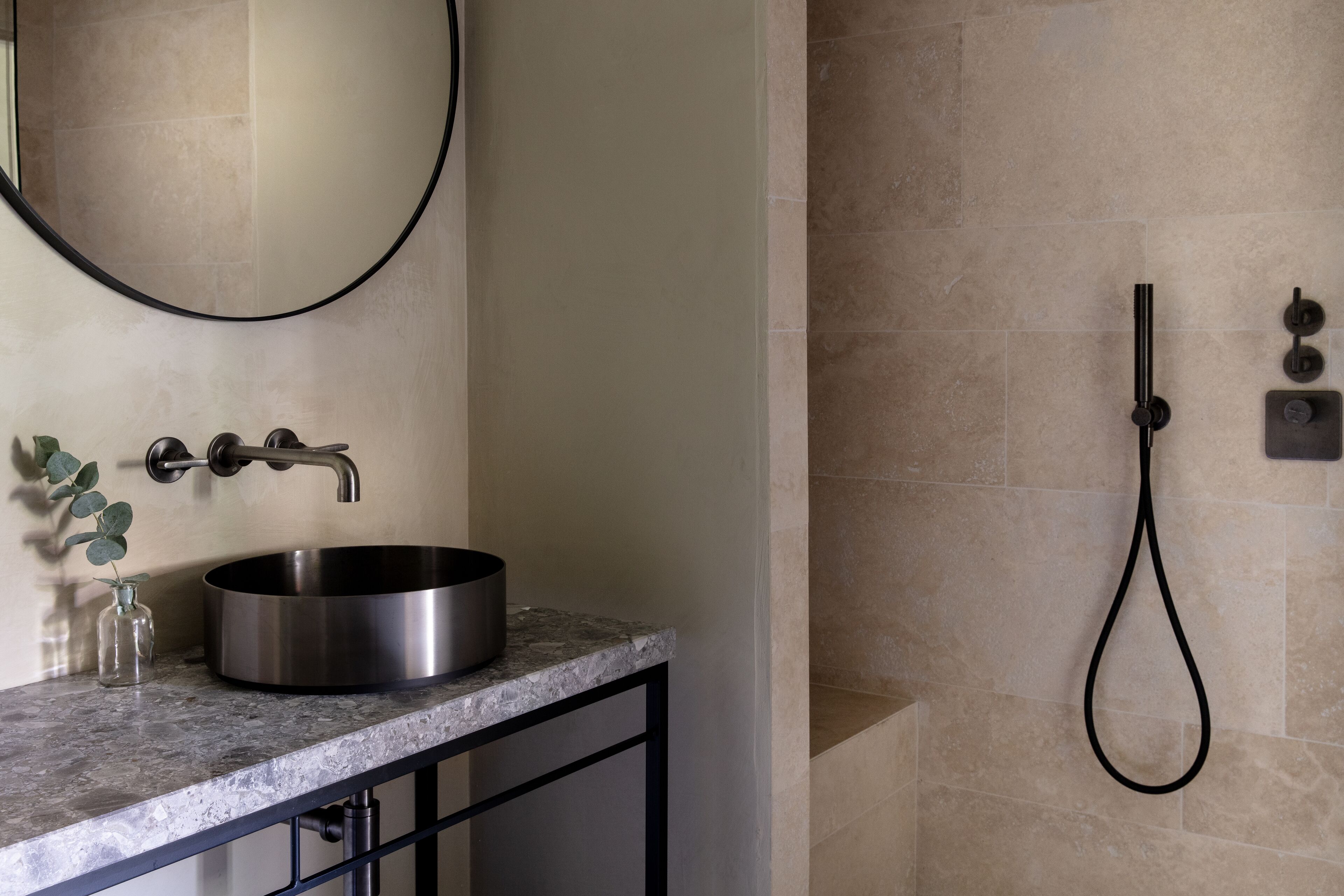 A bathroom with a round stainless steel sink, a mirror, and a handheld showerhead.