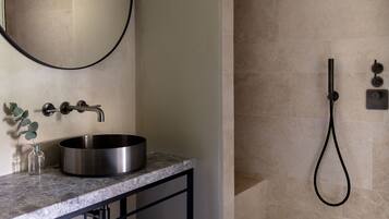 A bathroom with a round stainless steel sink, a mirror, and a handheld showerhead.
