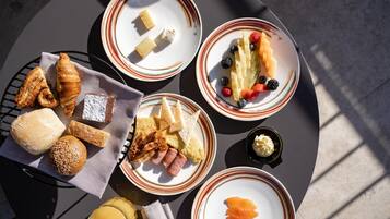 Una mesa redonda con una bandeja de desayuno que incluye croissants, pan, queso, jamón y fruta.