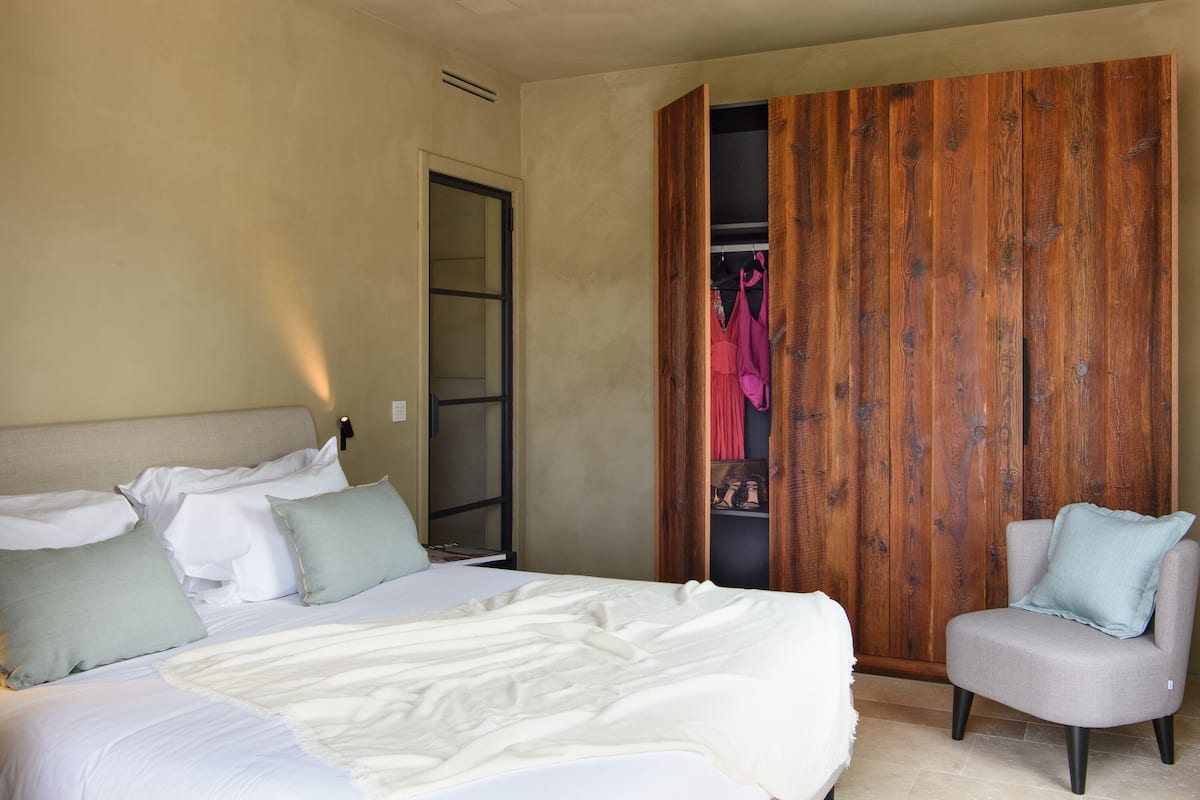Een slaapkamer met een bed, een stoel, een houten garderobe en een deur naar een inloopkast.