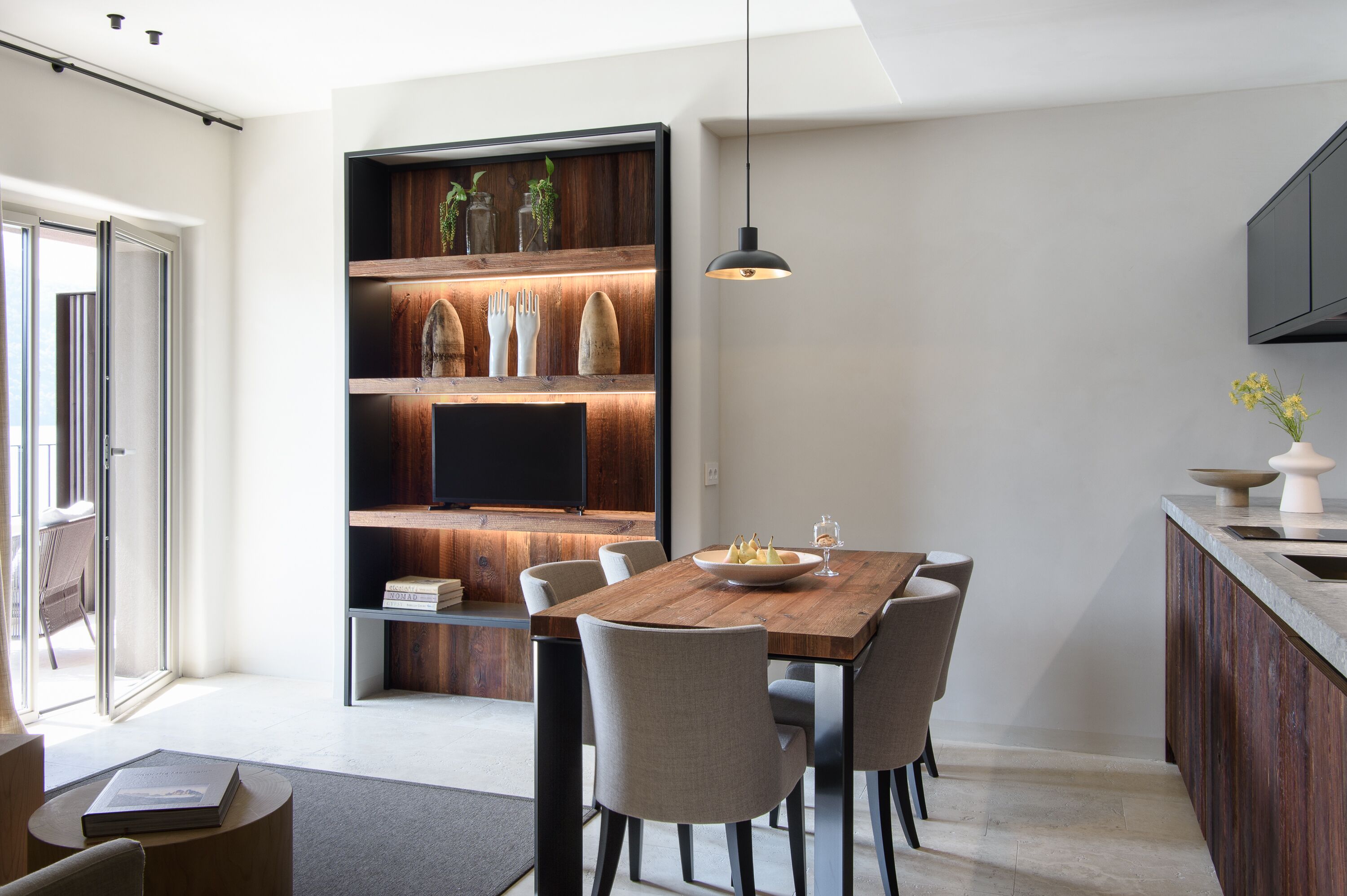 Zona pranzo moderna con tavolo in legno, sei sedie e una libreria a muro con oggetti decorativi.