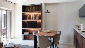 Zona pranzo moderna con tavolo in legno, sei sedie e una libreria a muro con oggetti decorativi.
