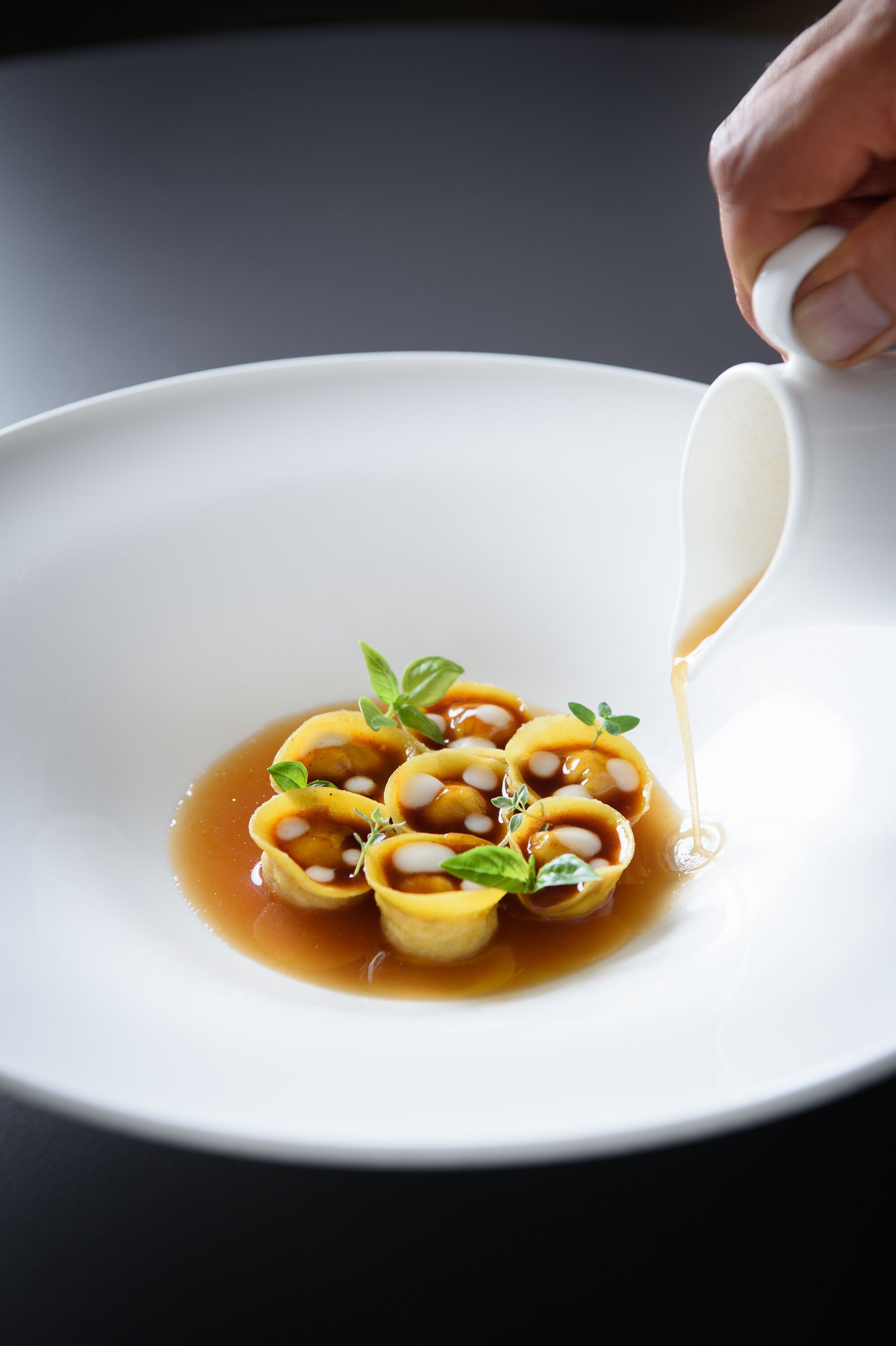 A white plate with ravioli and sauce, garnished with basil leaves.