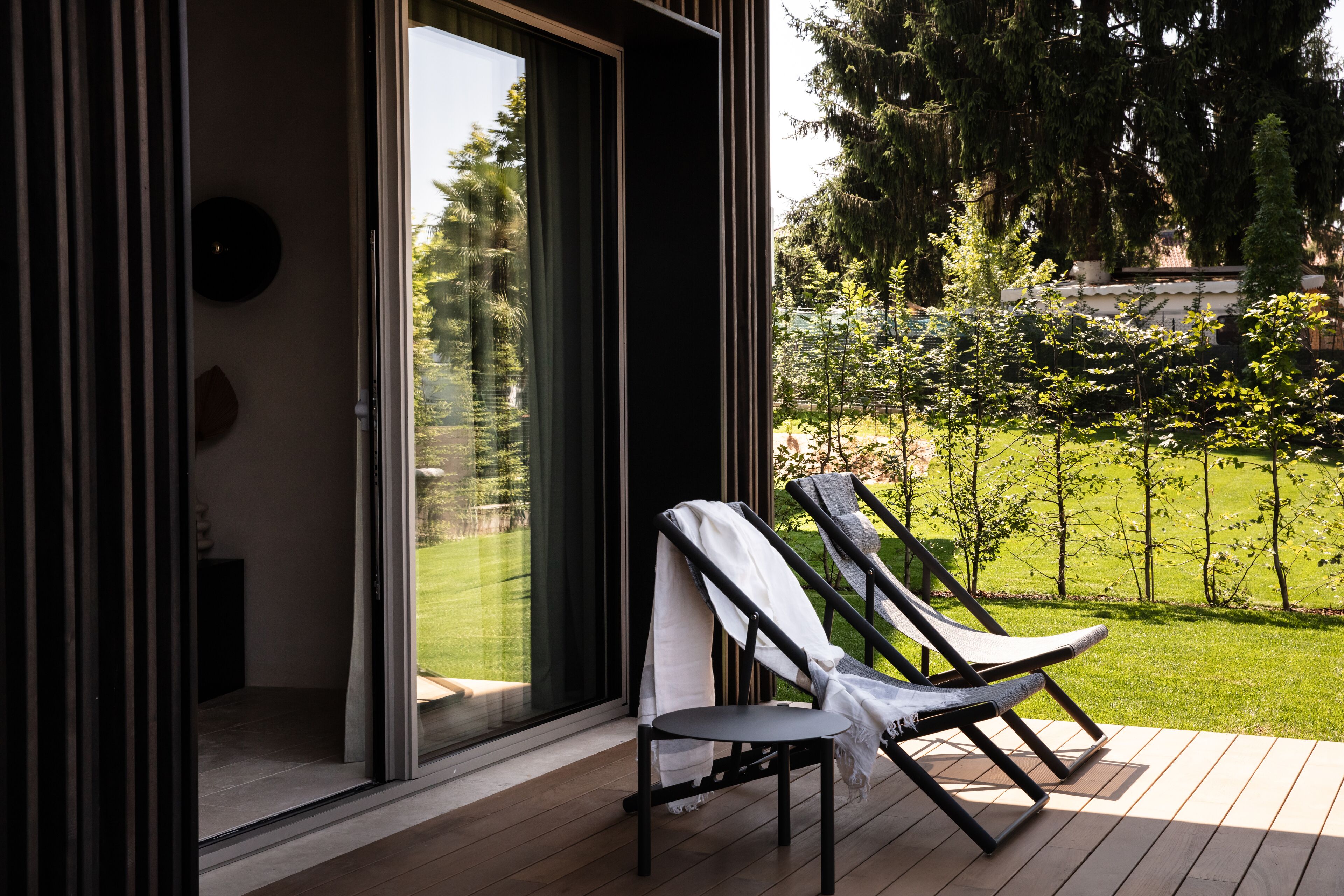 Een moderne buitenruimte met twee loungestoelen en een glazen deur naar een tuin.