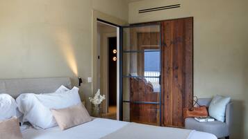 A bedroom with a bed, a grey armchair, a wooden door, and a view through the door.