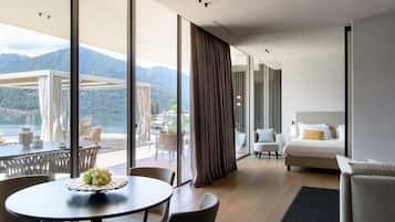 A modern hotel room with a balcony, a bed, a seating area, and a view of the mountains.