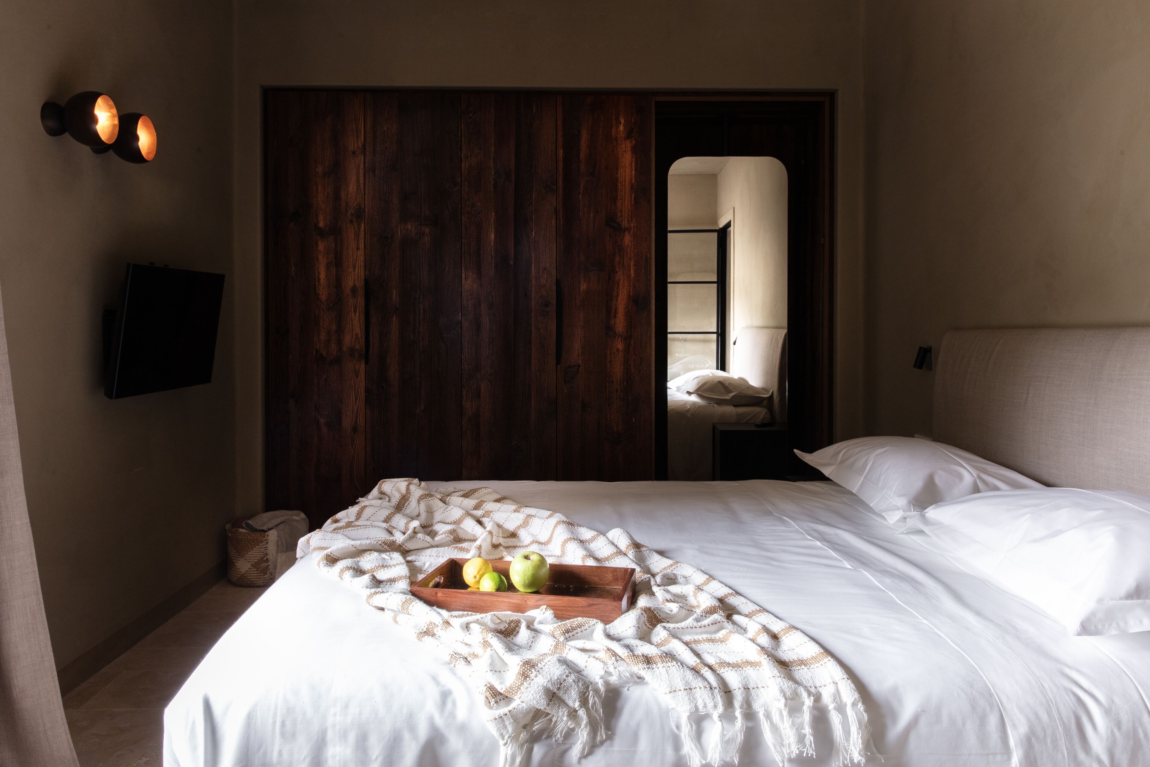 Una cama bien hecha con una colcha blanca y una bandeja de madera con manzanas.
