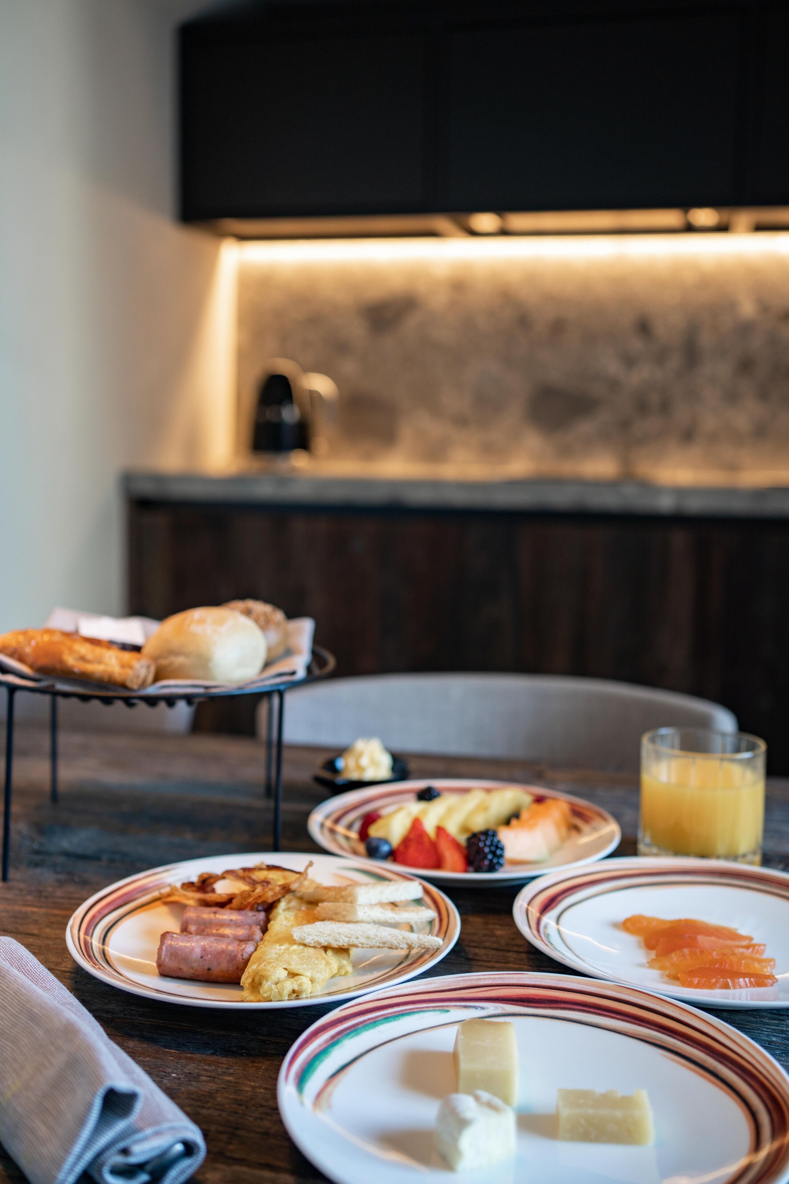 A breakfast setting with plates of food, a glass of orange juice, and a napkin on a wooden table.