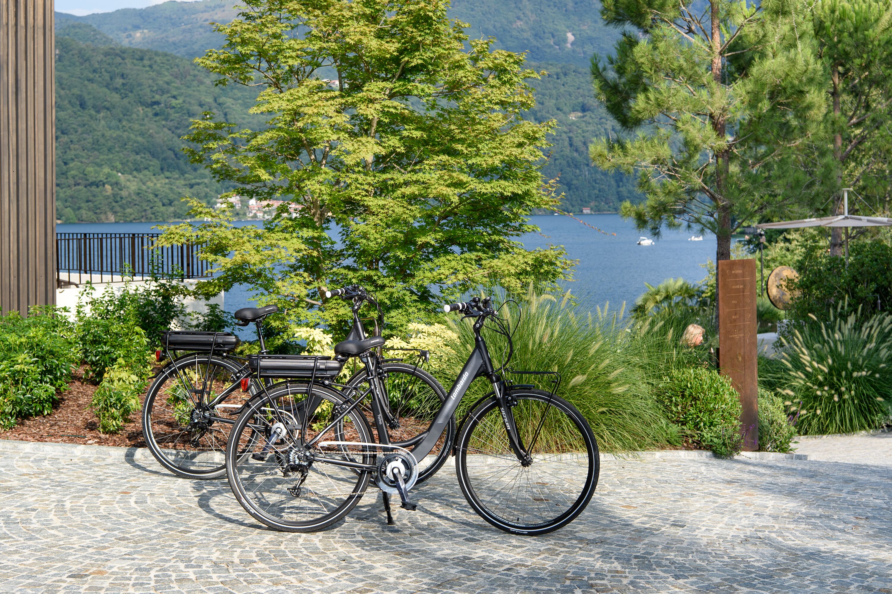 A bicycle parked on a cobblestone path with a view of a lake and mountains in the background.