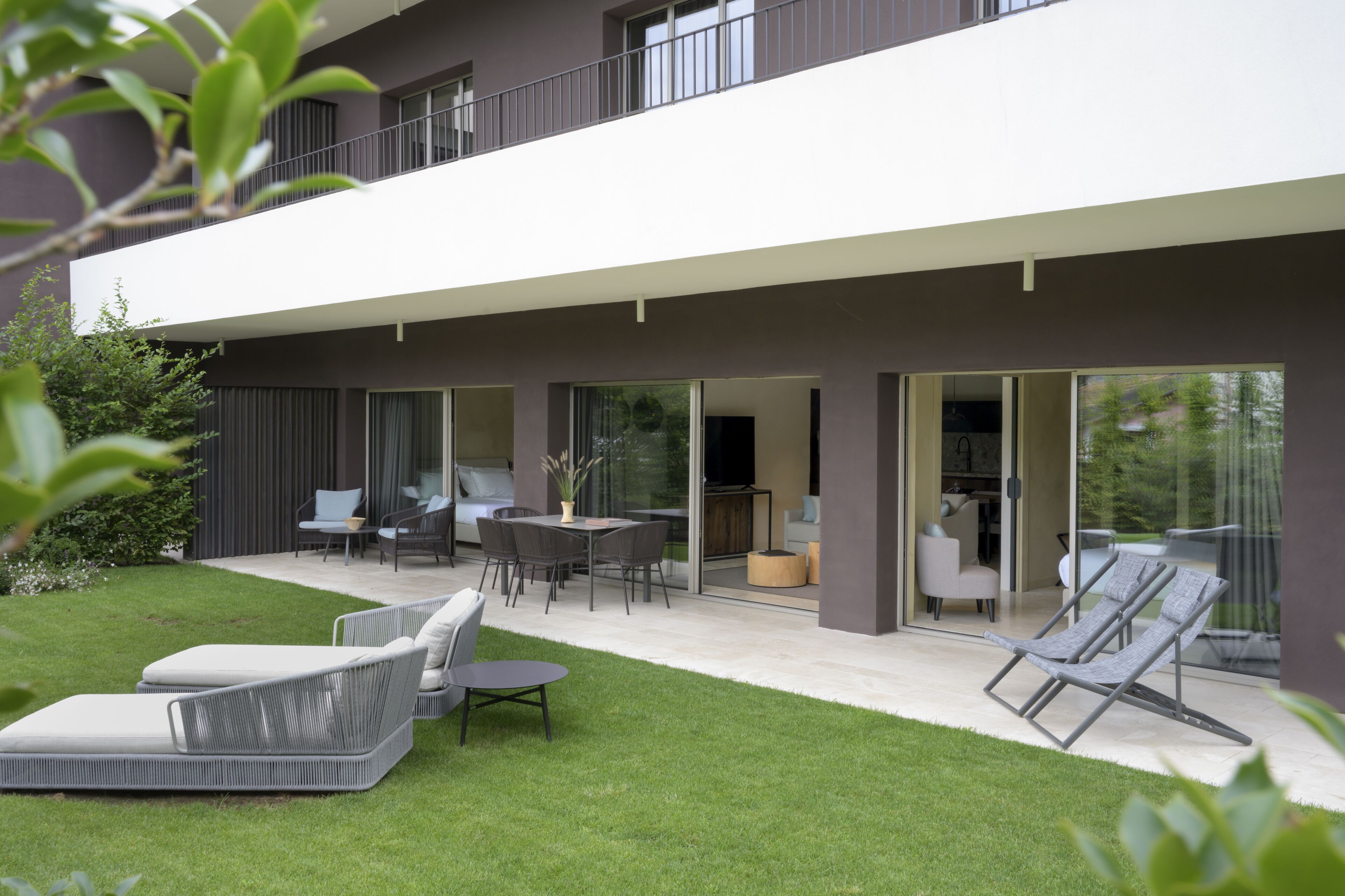Ein modernes, zweistöckiges Haus mit Terrasse, Gartenmöbeln und Rasenfläche.