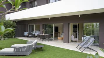Ein modernes, zweistöckiges Haus mit Terrasse, Gartenmöbeln und Rasenfläche.