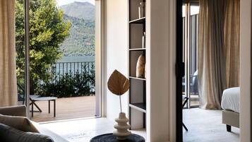 Ein modernes Hotelzimmer mit Balkon, Blick auf einen See und Berge, einem großen Fenster und einem Bett.