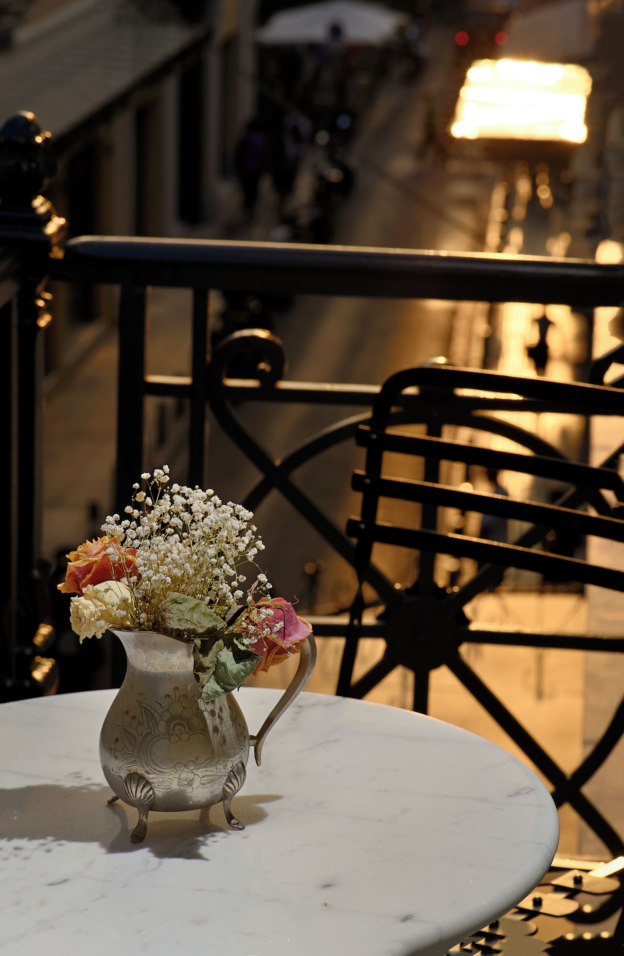 A table with a decorative vase containing flowers, set on a balcony with a railing.