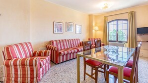 A living room with a striped sofa set, a glass-top dining table, and a television on the wall. - GuestHost - Molino Stucky Residence Bragosso Suite (Venezia)
