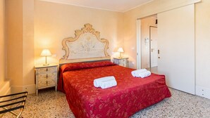 A hotel room with a bed, two bedside tables with lamps, a door, and a chair. - GuestHost - Molino Stucky Residence Bragosso Suite (Venezia)