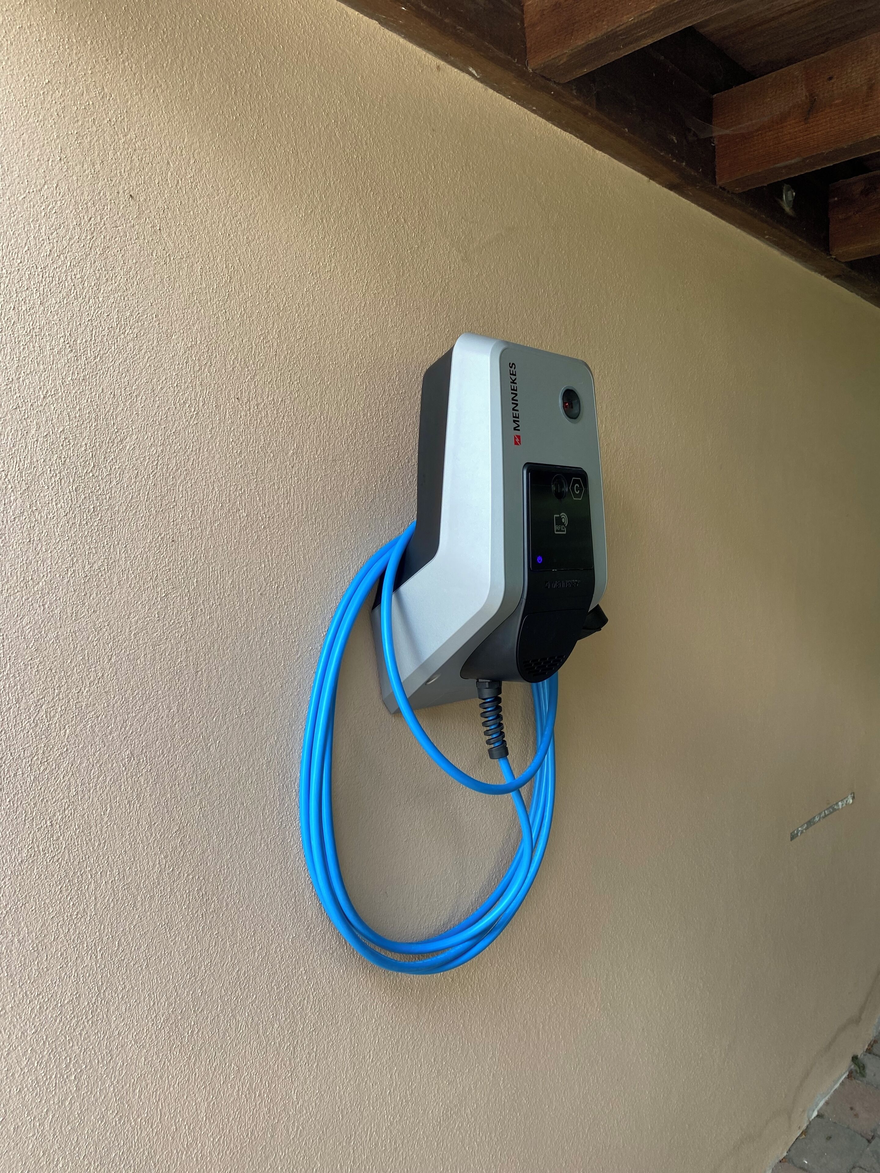 A device mounted on a textured wall with a blue cable connected to it.